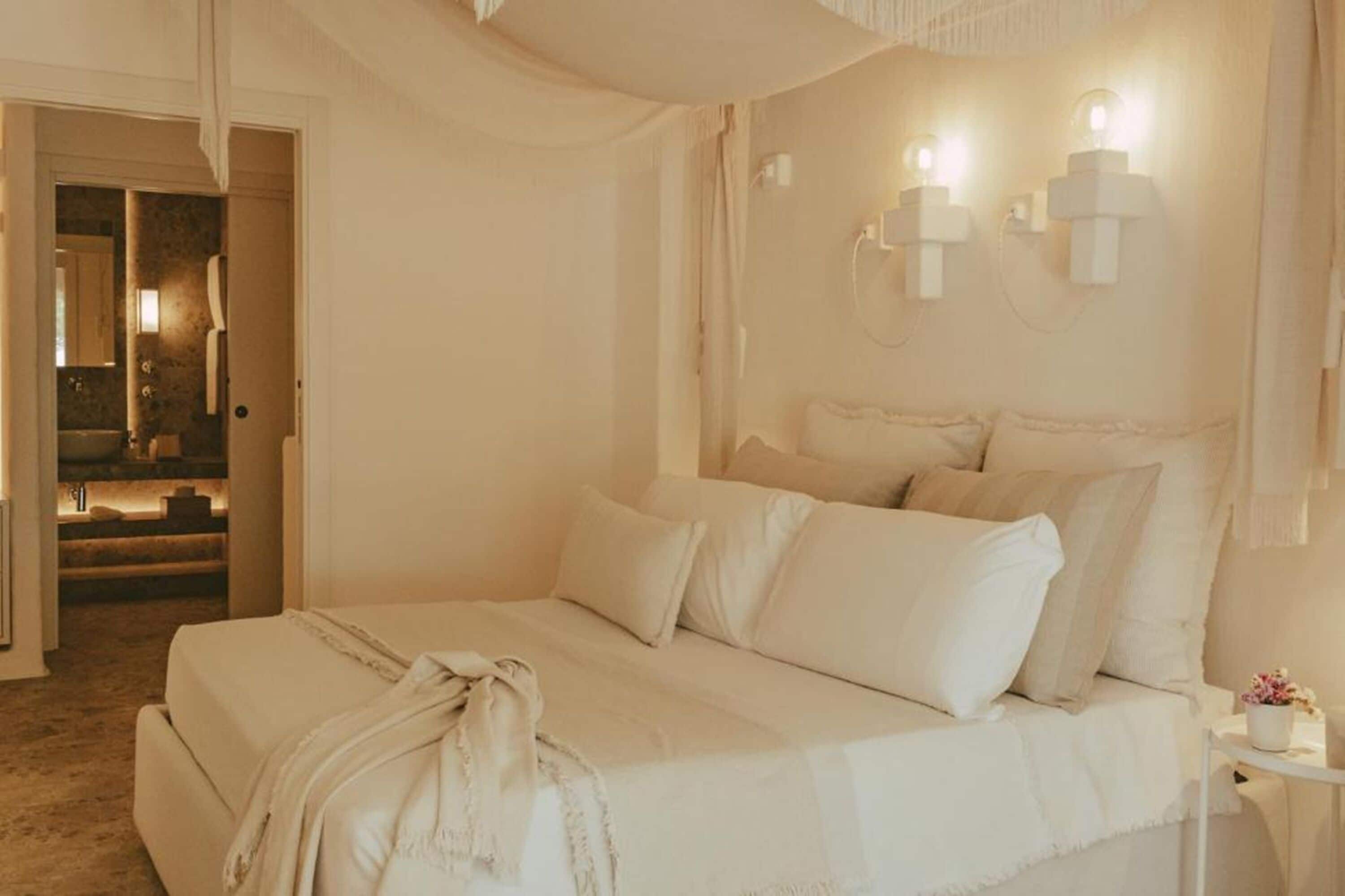 A bedroom with a large bed, a bedside table with a lamp, and a view of a bathroom.