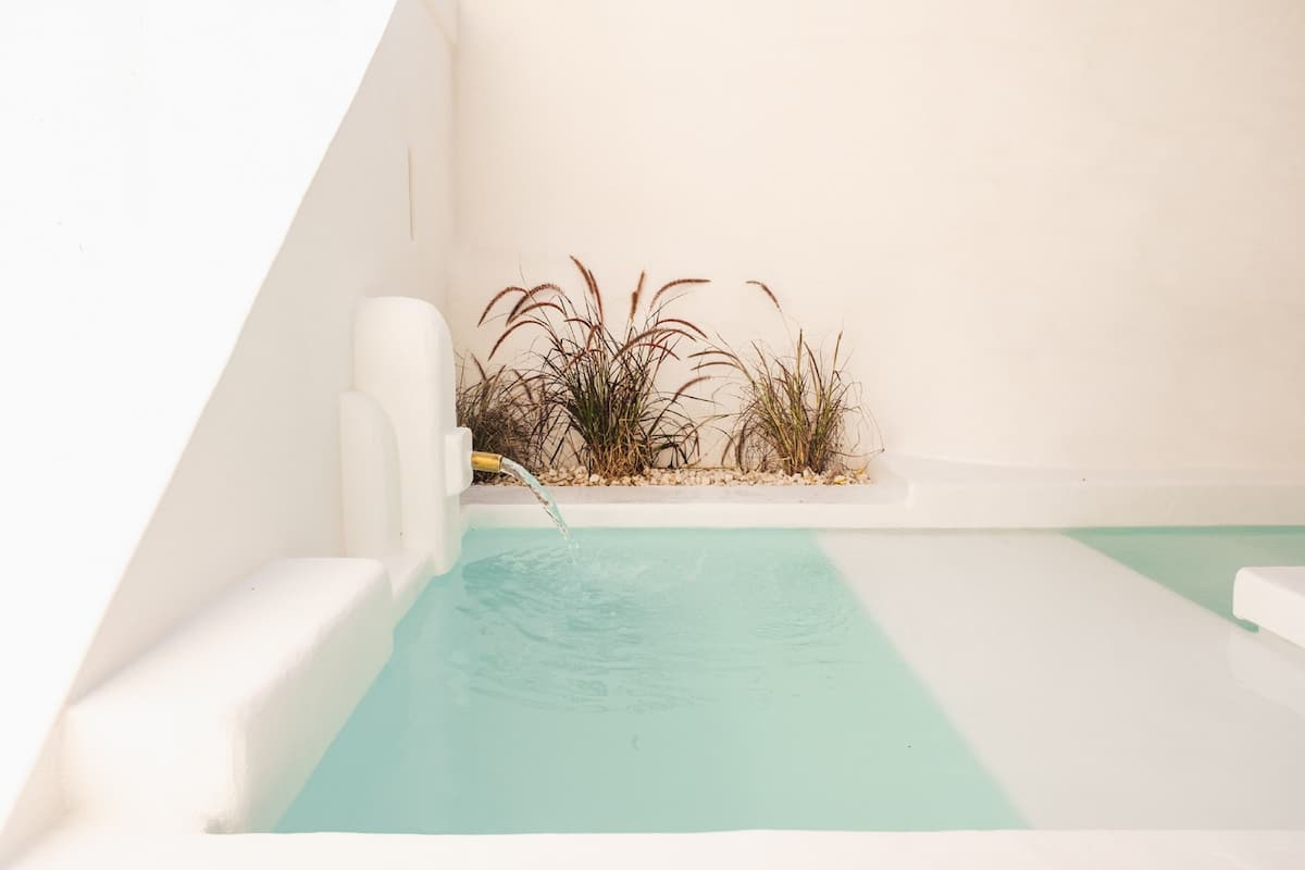 Ein kleiner, privater Pool mit klarem, blauem Wasser, umgeben von einer weißen Mauer und einer kleinen Pflanzfläche.