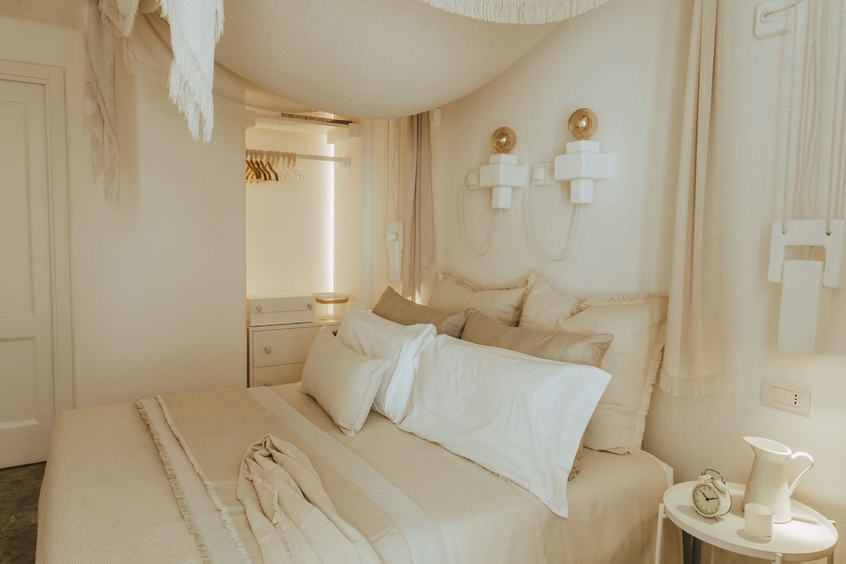 A bedroom with a large bed, bedside tables, a nightstand, and a wall-mounted light fixture.