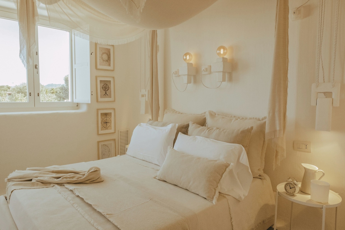 A bedroom with a bed, a bedside table with a clock and a cup, and wall-mounted light fixtures.