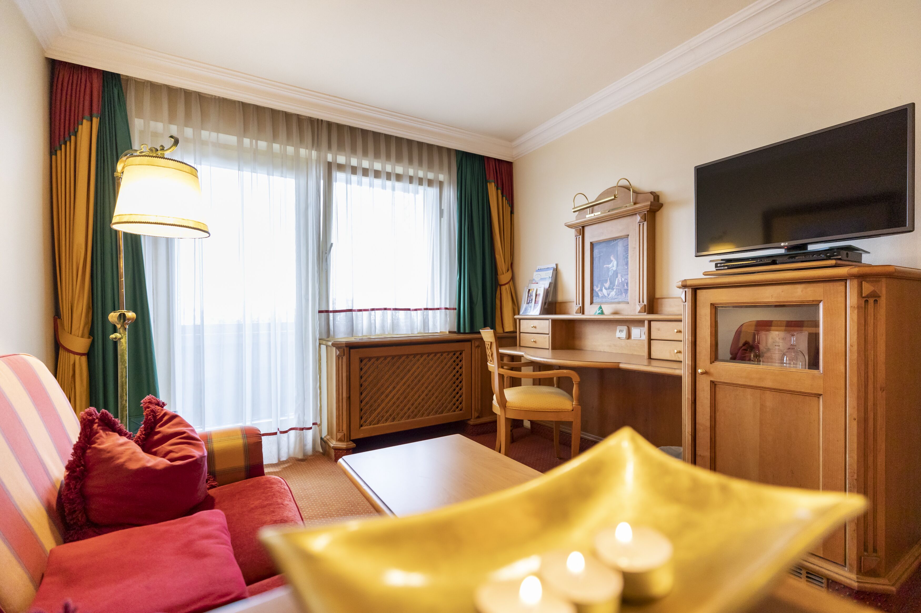 A hotel room with a sofa, a desk, a television, and a cabinet.