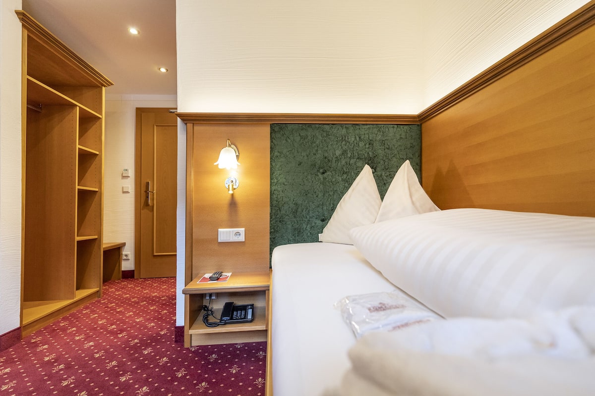 Ein Hotelzimmer mit einem Bett, einem Holzschrank, einem Nachttisch mit Lampe und einem grünen Kopfteil.