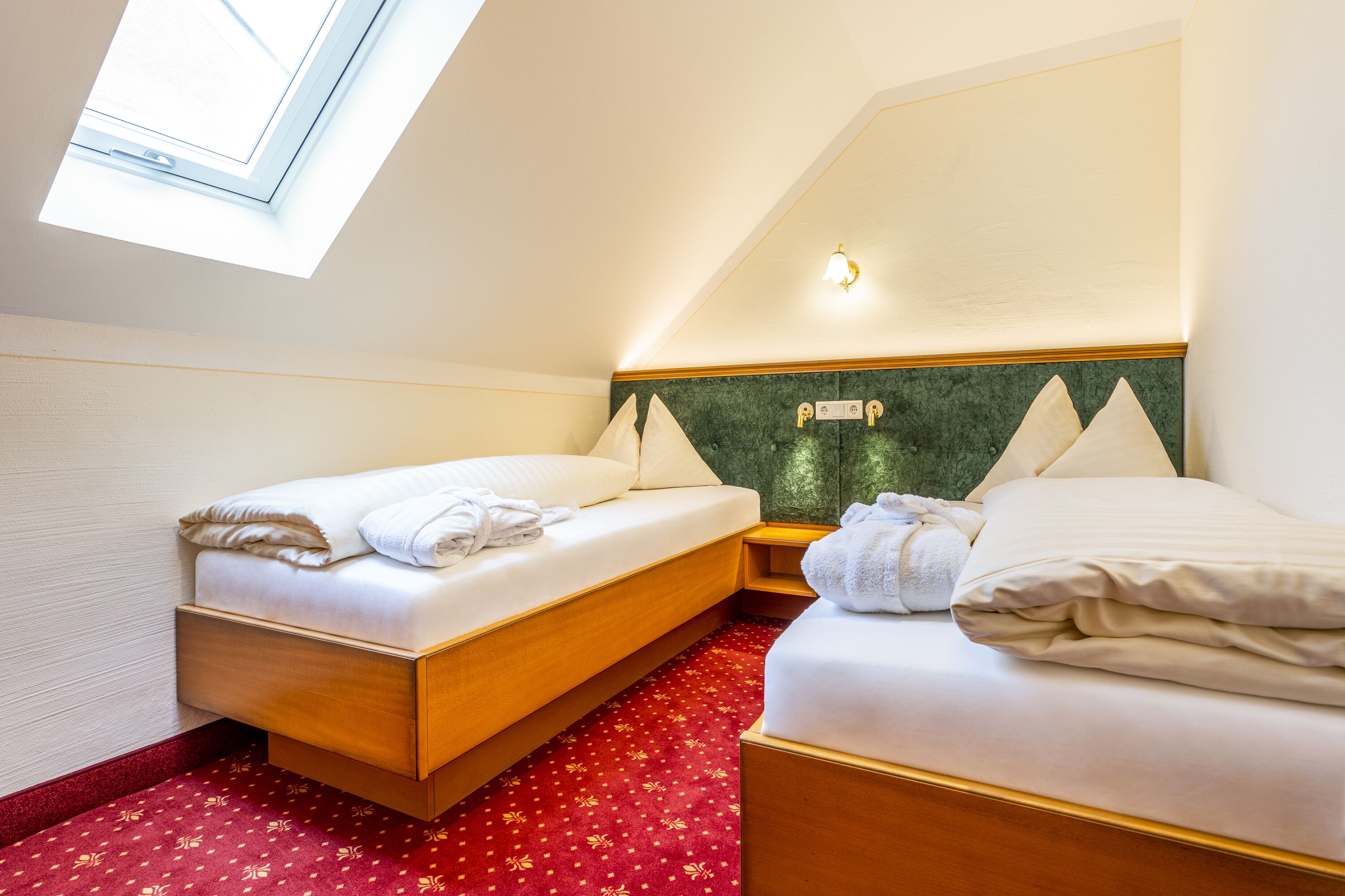 A hotel room with two beds, a skylight, a green headboard, and a red carpet.