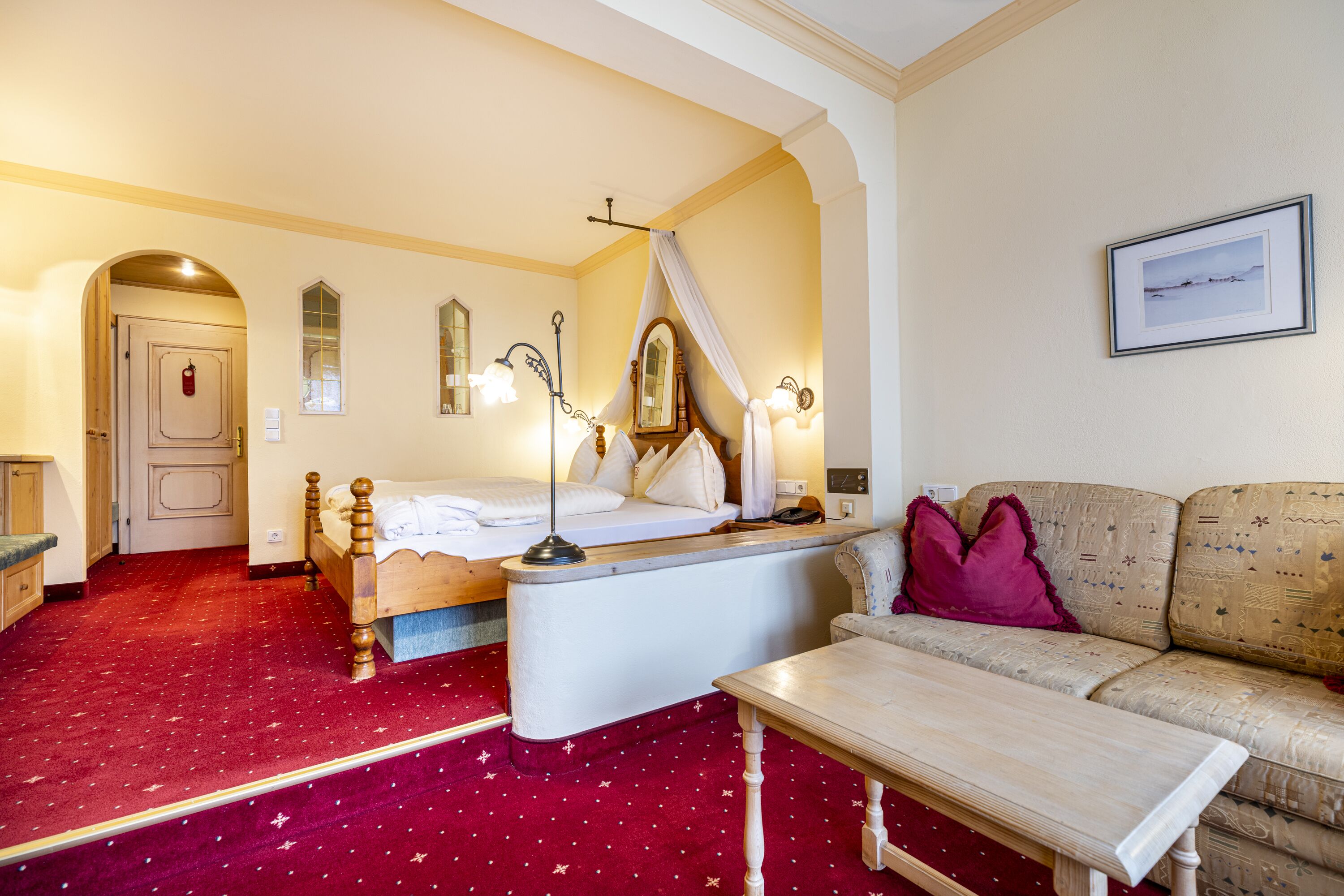 A hotel room with a bed, a nightstand, a table, a sofa, and a mirror.