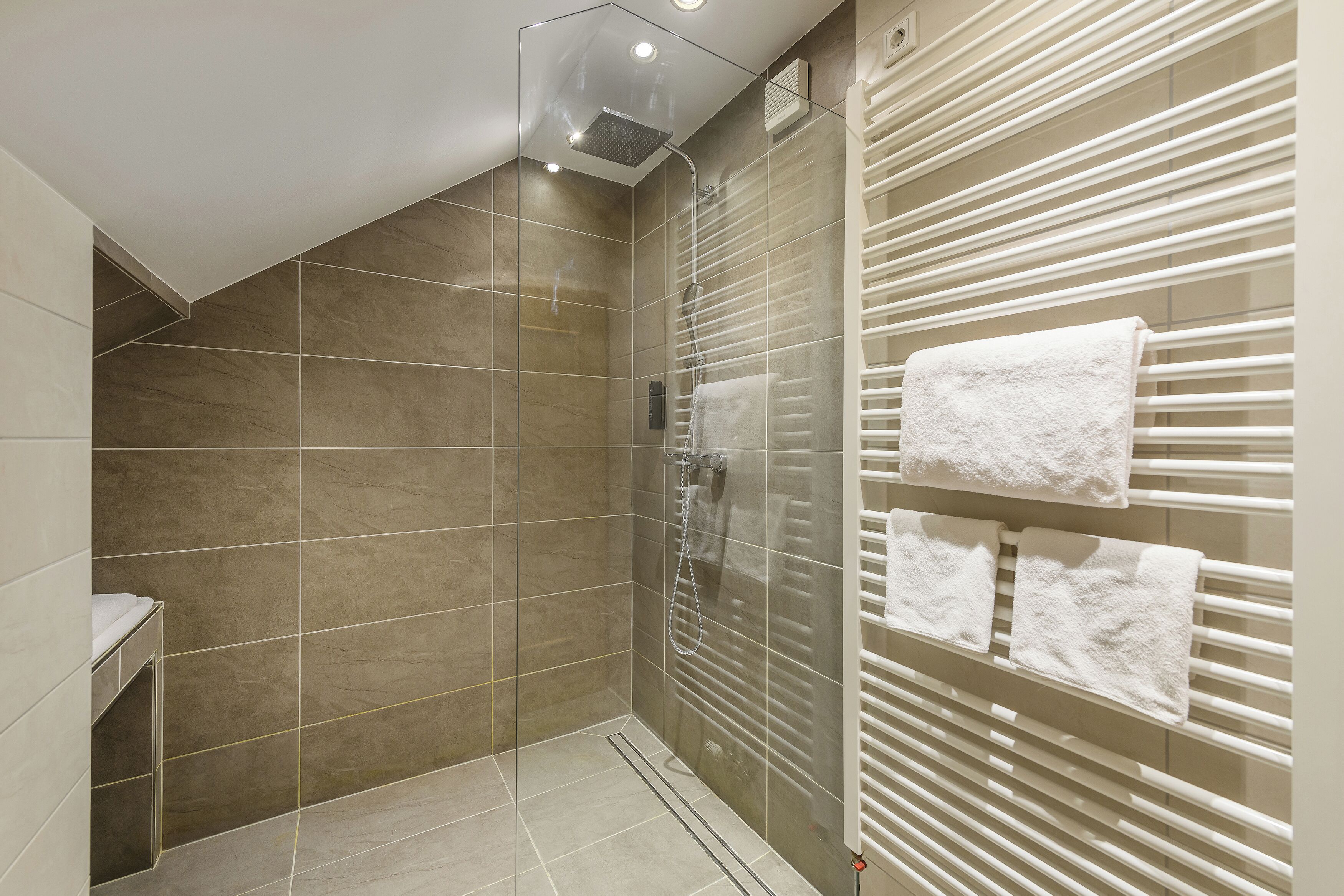 Un baño moderno con cabina de ducha de vidrio, un perchero con varias toallas y suelo de baldosas.