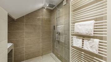 Un baño moderno con cabina de ducha de vidrio, un perchero con varias toallas y suelo de baldosas.