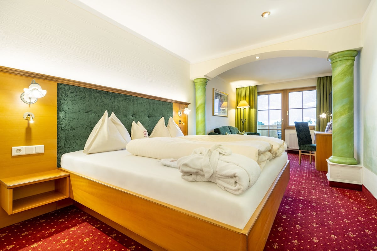 Ein Hotelzimmer mit einem großen Bett, einem Schreibtisch, einem Sessel und Blick ins Freie.