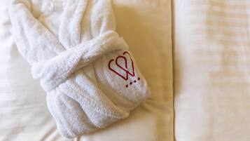 A white towel with a heart and stars embroidered on it, placed on a bed with a white and beige patterned bedspread.