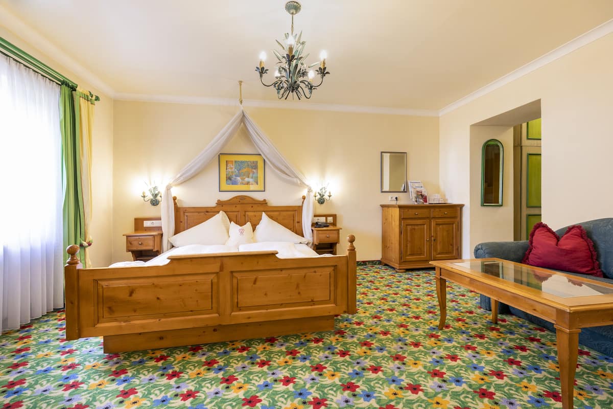 Ein Schlafzimmer mit einem hölzernen Bett, einem Glastisch und einem farbenfrohen Teppich mit floralem Muster.