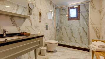 Un baño moderno con suelo de mármol, ducha con cerramiento de vidrio, inodoro y tocador con espejo y teléfono.