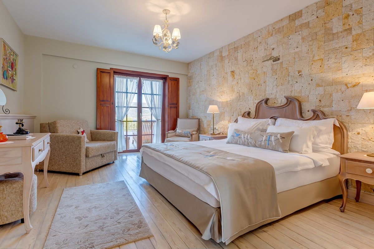 A bedroom with a large bed, a wooden nightstand, a chair, a desk, and a chandelier.