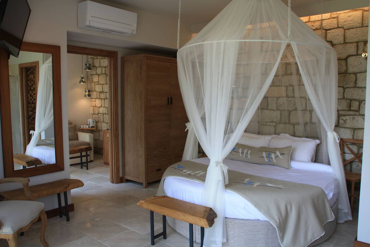 A bedroom with a four-poster bed, a wooden bench, a mirror, and a stone wall.