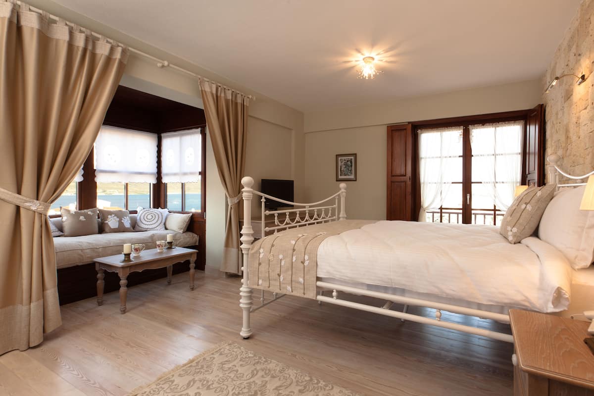 A bedroom with a large bed, a sofa, a small table, and a view of the sea through the windows.