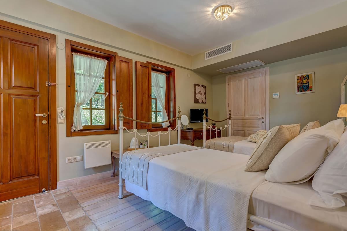 A bedroom with a bed, a dresser, a television, and a window with curtains.