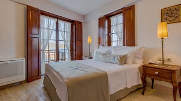A hotel room with a large bed, two bedside tables, a nightstand, a window with curtains, and a radiator.