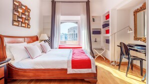 Une chambre d’hôtel avec un grand lit, un bureau, une chaise, une bibliothèque et une vue sur un bâtiment historique.