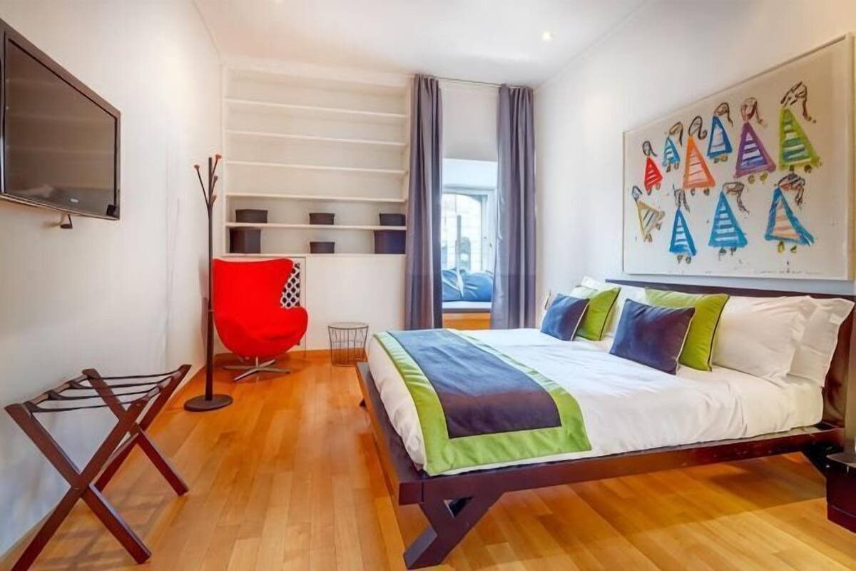 A bedroom with a bed, a red chair, a TV, and a window.