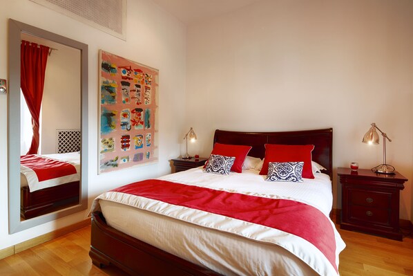 A neatly arranged bedroom with a large bed, a bedside table with a lamp, and a wall-mounted artwork.