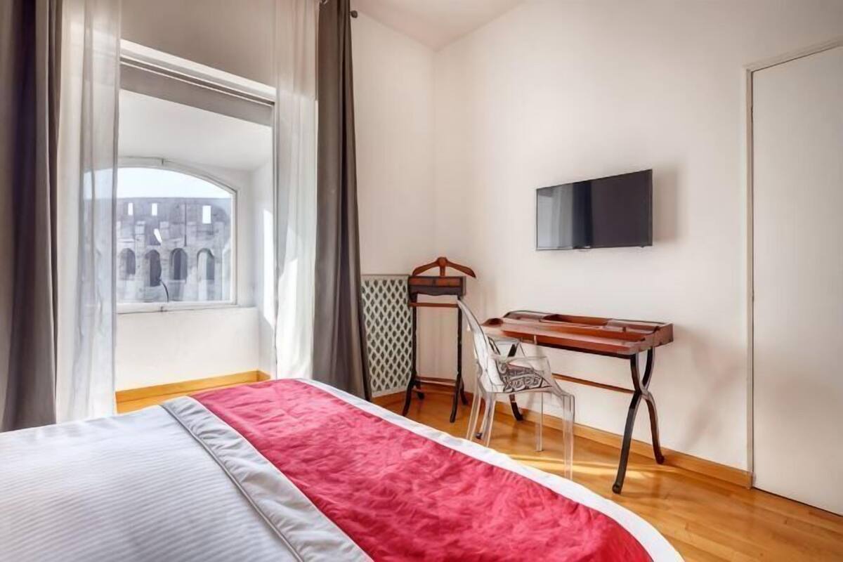 A hotel room with a bed, a desk, a chair, a TV, and a window with curtains.