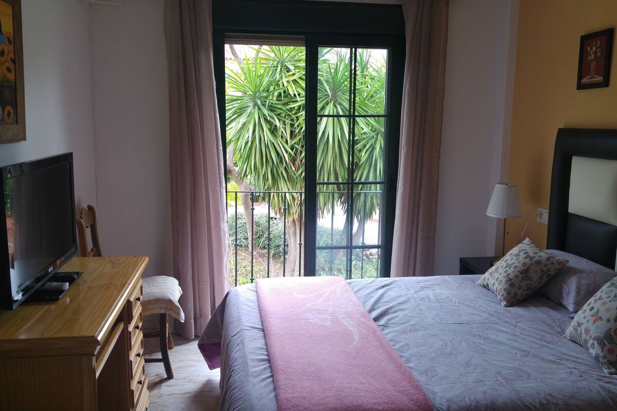 A bedroom with a bed, a desk, a television, and a window with curtains.