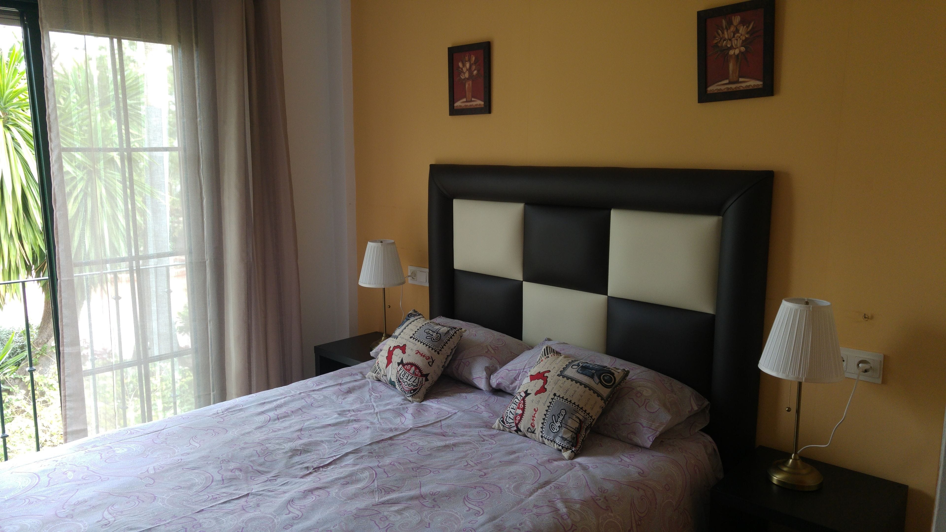 Une chambre à coucher comprenant un lit, deux tables de chevet, une fenêtre avec des rideaux et deux lampes fixées au mur.