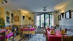A dining area with tables set for a meal, featuring a large window with curtains, framed pictures on the walls, and a chandelier. - Hospederia V Centenario (Estepona)
