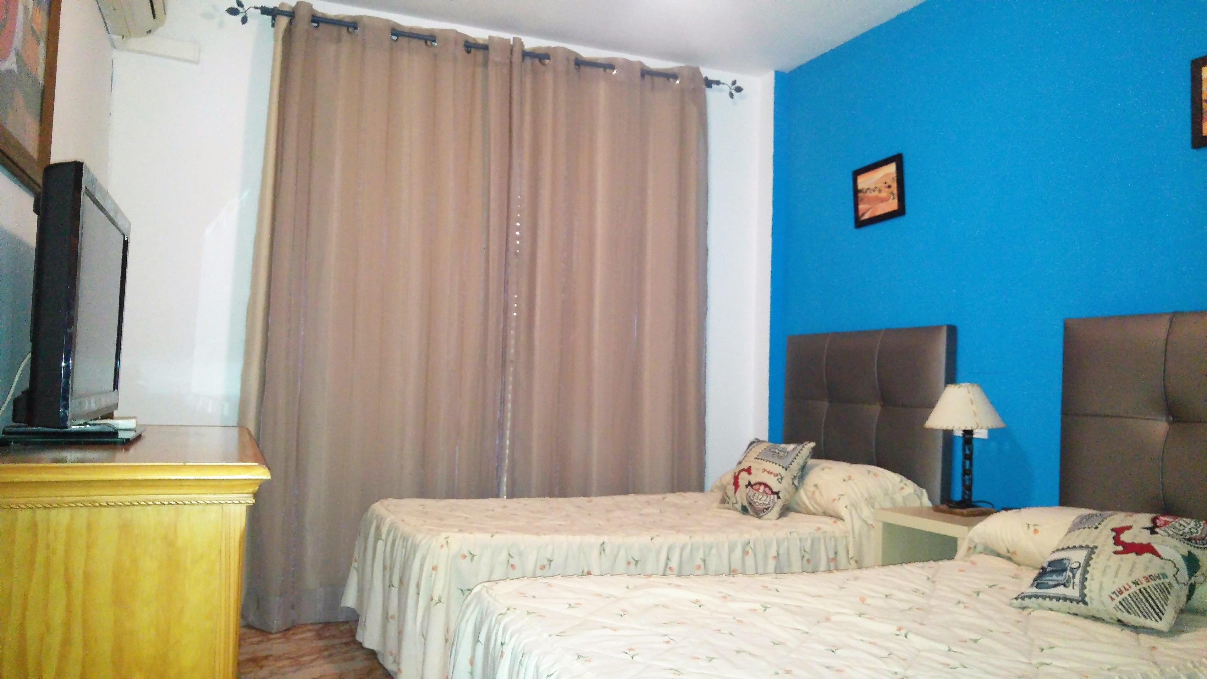 Una habitación de hotel con dos camas, un televisor sobre un mueble de madera, una pared azul y una cortina.