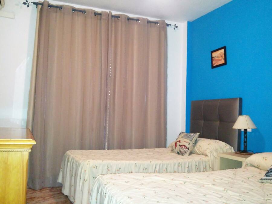 Una habitación de hotel con dos camas, un televisor sobre un mueble de madera, una pared azul y una cortina.