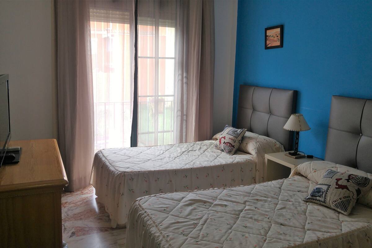 A bedroom with two beds, a desk, a television, and a window with curtains.