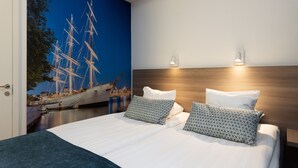 Une chambre à coucher moderne avec un grand lit, deux oreillers, une tête de lit en bois et une fresque murale représentant un navire à voile.