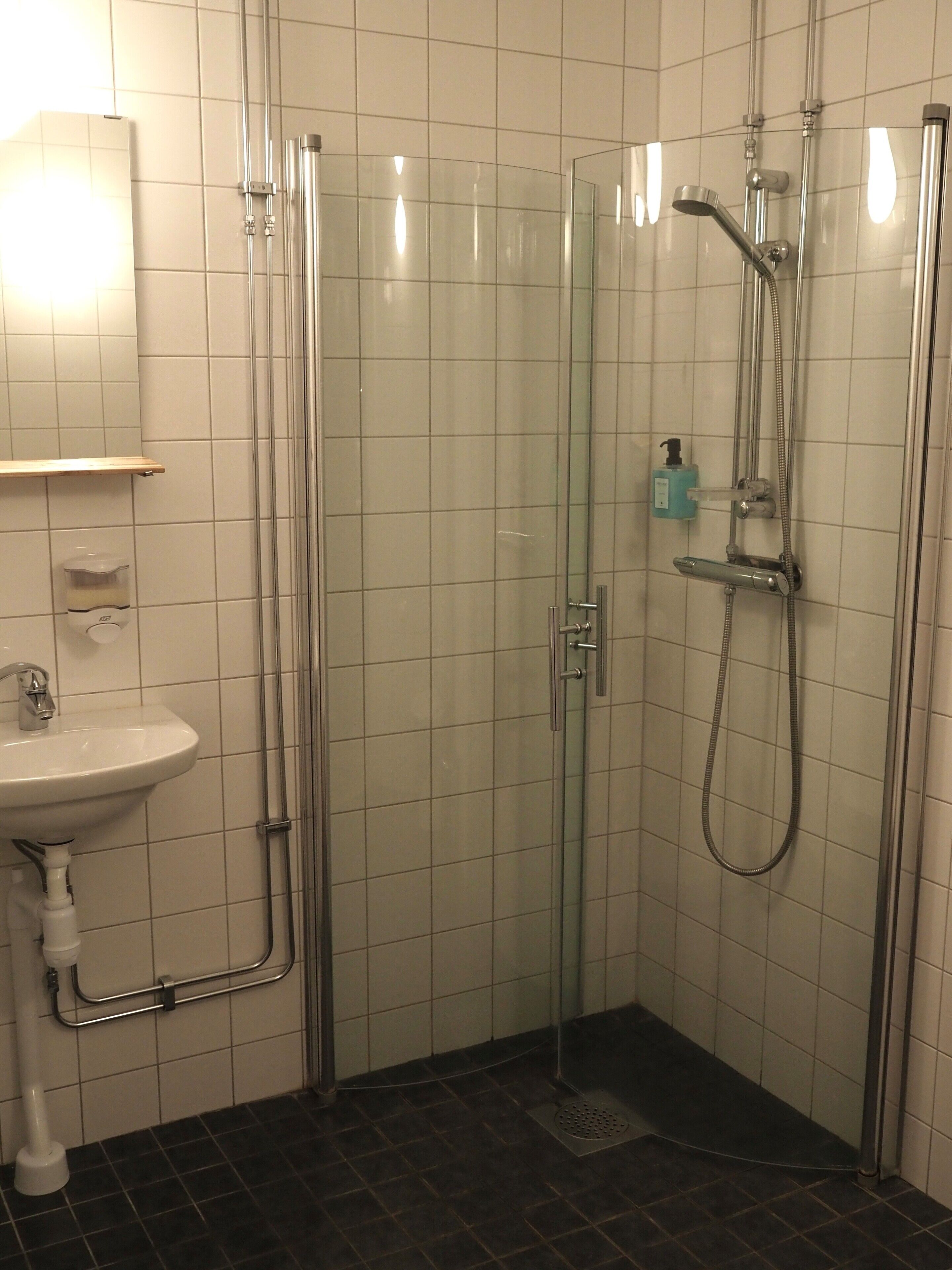 Un baño con ducha de vidrio, un lavamanos y dispensador de jabón.