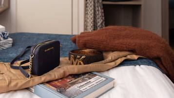 A bed with a book, a bag, and a pillow. A closet with clothes and shoes is in the background.