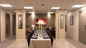 Une salle de conférence avec une longue table préparée pour une réunion, entourée de chaises, d’un canapé et d’un écran de télévision diffusant une image de feu.