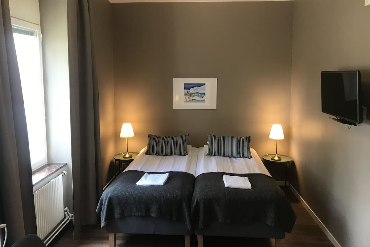 A double bed with two pillows, a bedside lamp, a framed picture on the wall, and a TV mounted on the wall.