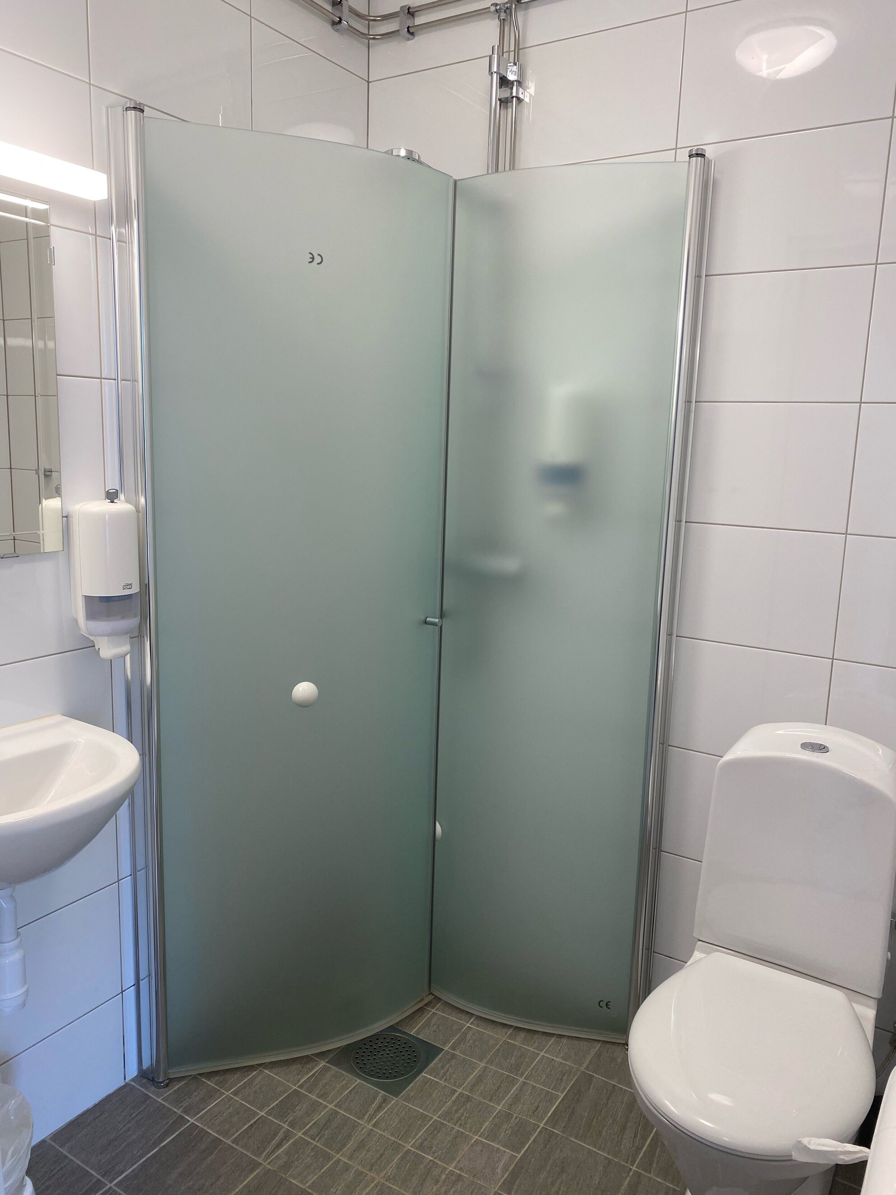 A corner bathroom with a glass partition, a sink, and a toilet.
