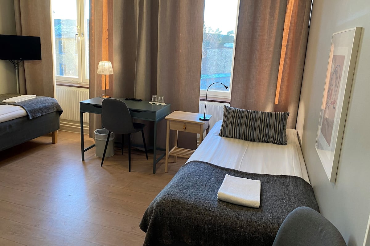 A hotel room with two beds, a desk, a chair, a TV, and a window with curtains.