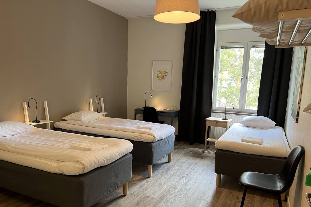 A hotel room with three beds, a desk, a chair, and a window with curtains.