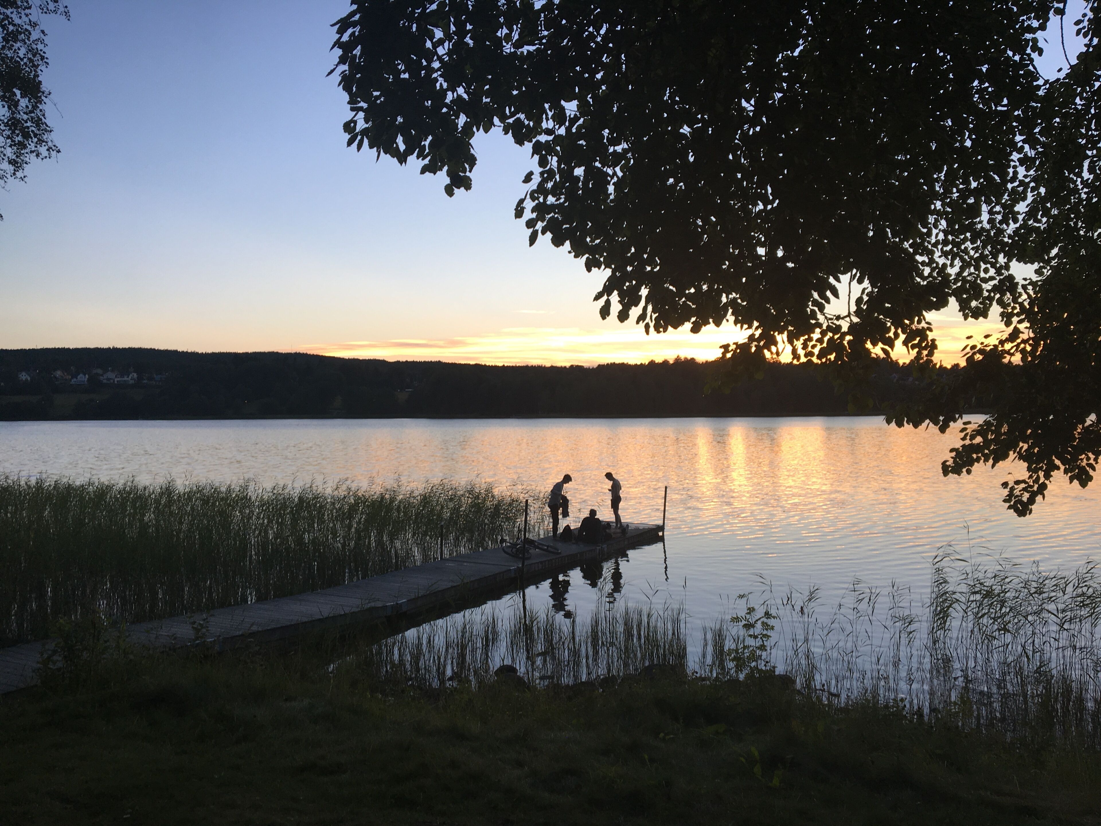 Un lago tranquilo al atardecer con un muelle y gente pescando.