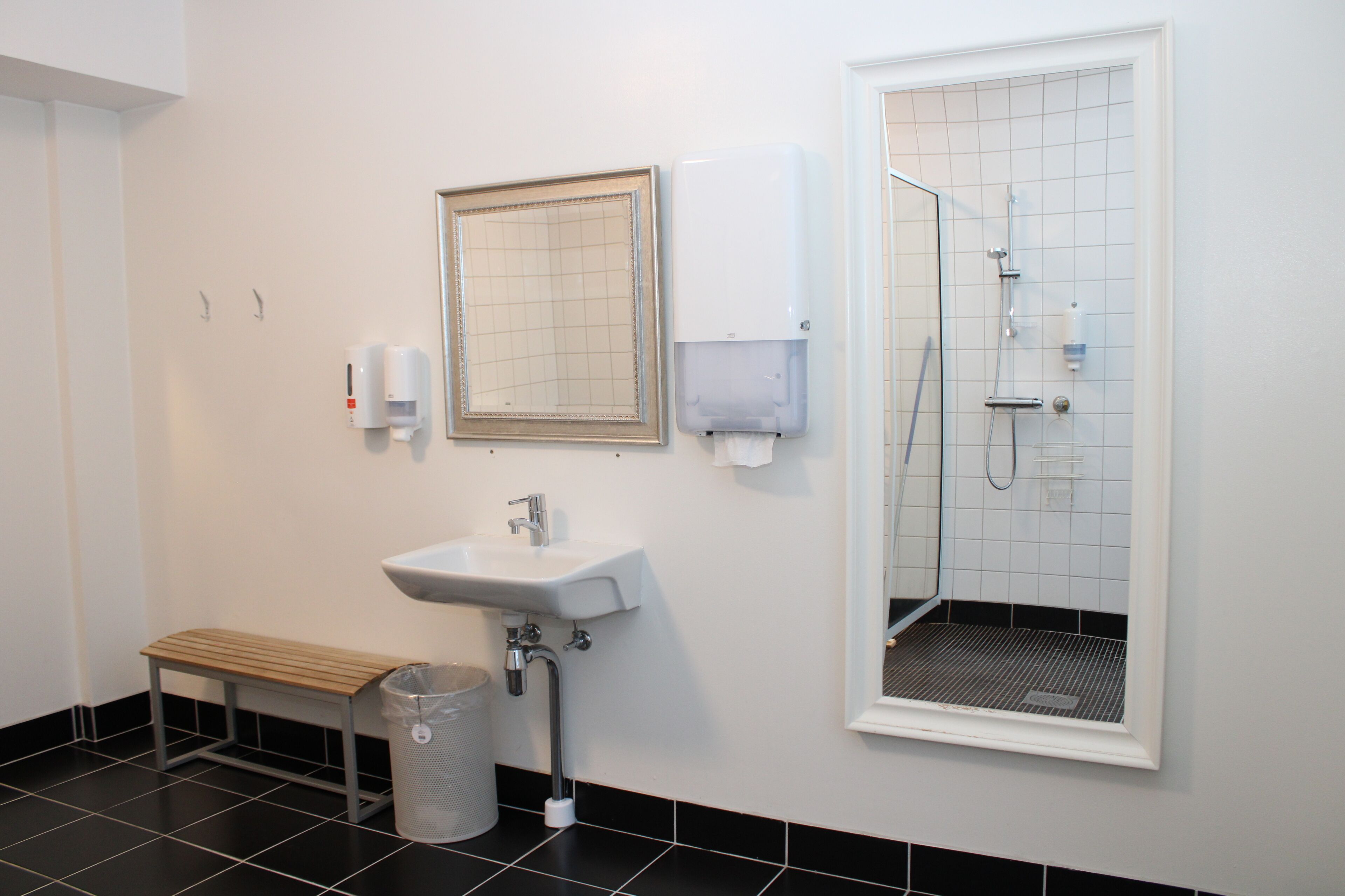 A bathroom with a sink, mirror, hand dryer, and shower.