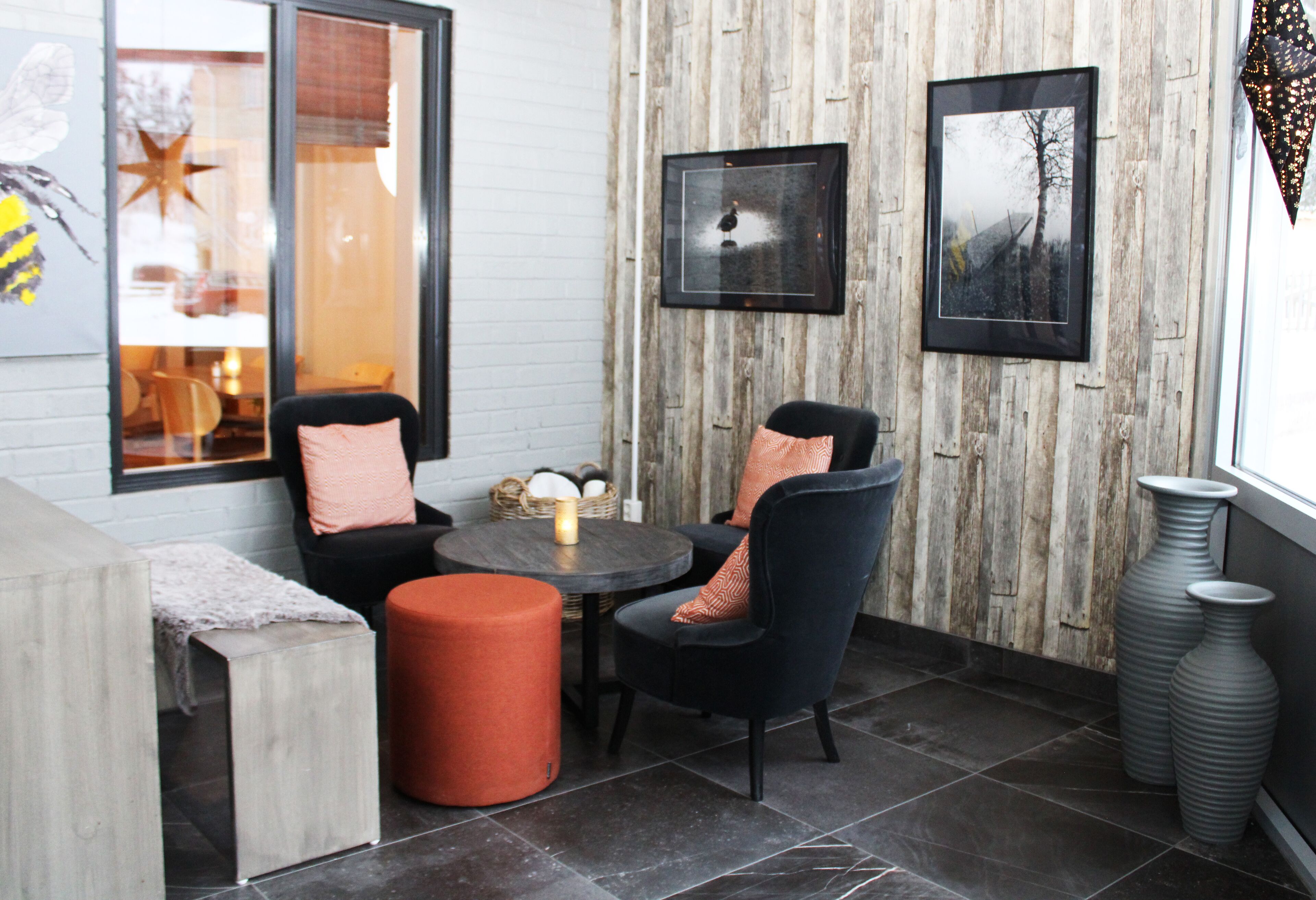 A cozy seating area with a round table, two chairs, and a small orange ottoman. There are framed pictures on the wall and a large window with a view.