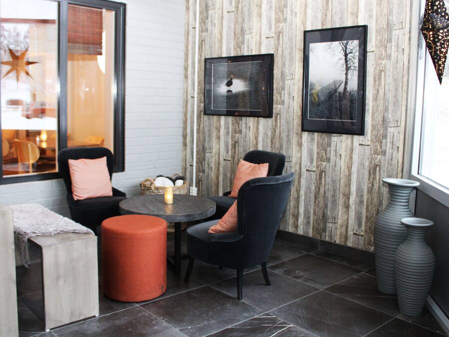 A cozy seating area with a round table, two chairs, and a small orange ottoman. There are framed pictures on the wall and a large window with a view.