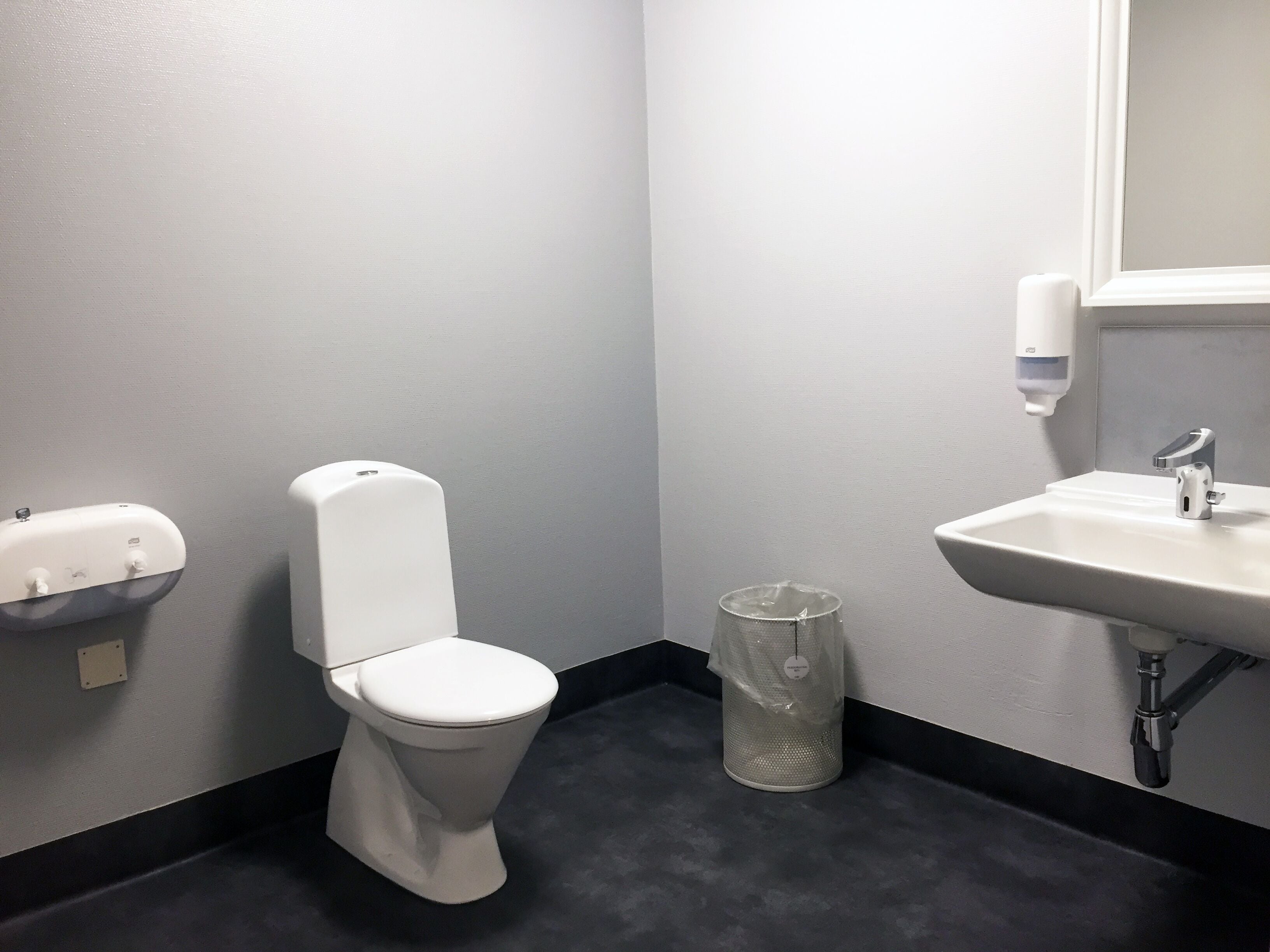 A small bathroom with a toilet, a sink, and a hand sanitizer dispenser.