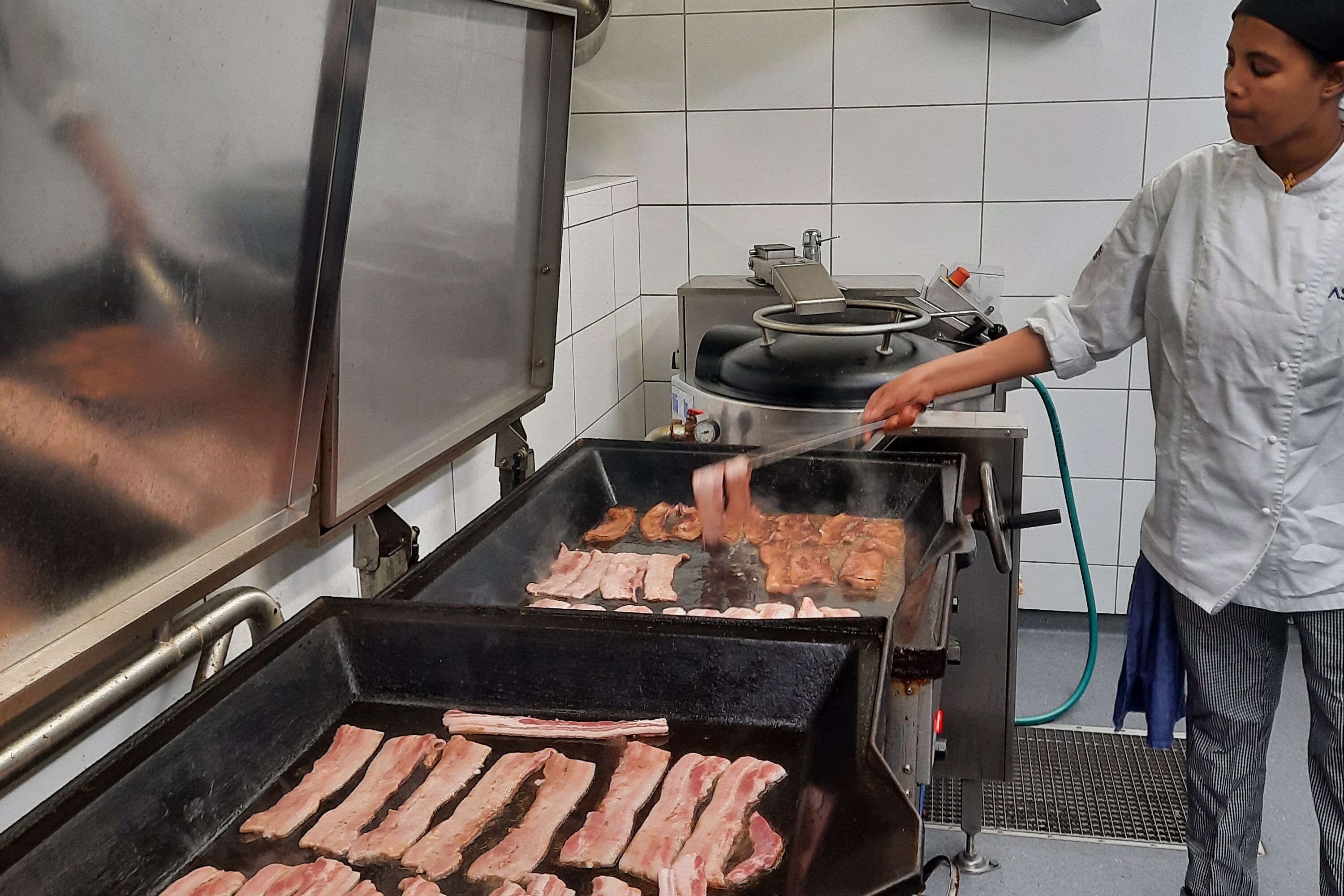 Ett kök med en stor grill, en person som lagar mat och en spis med kastruller.