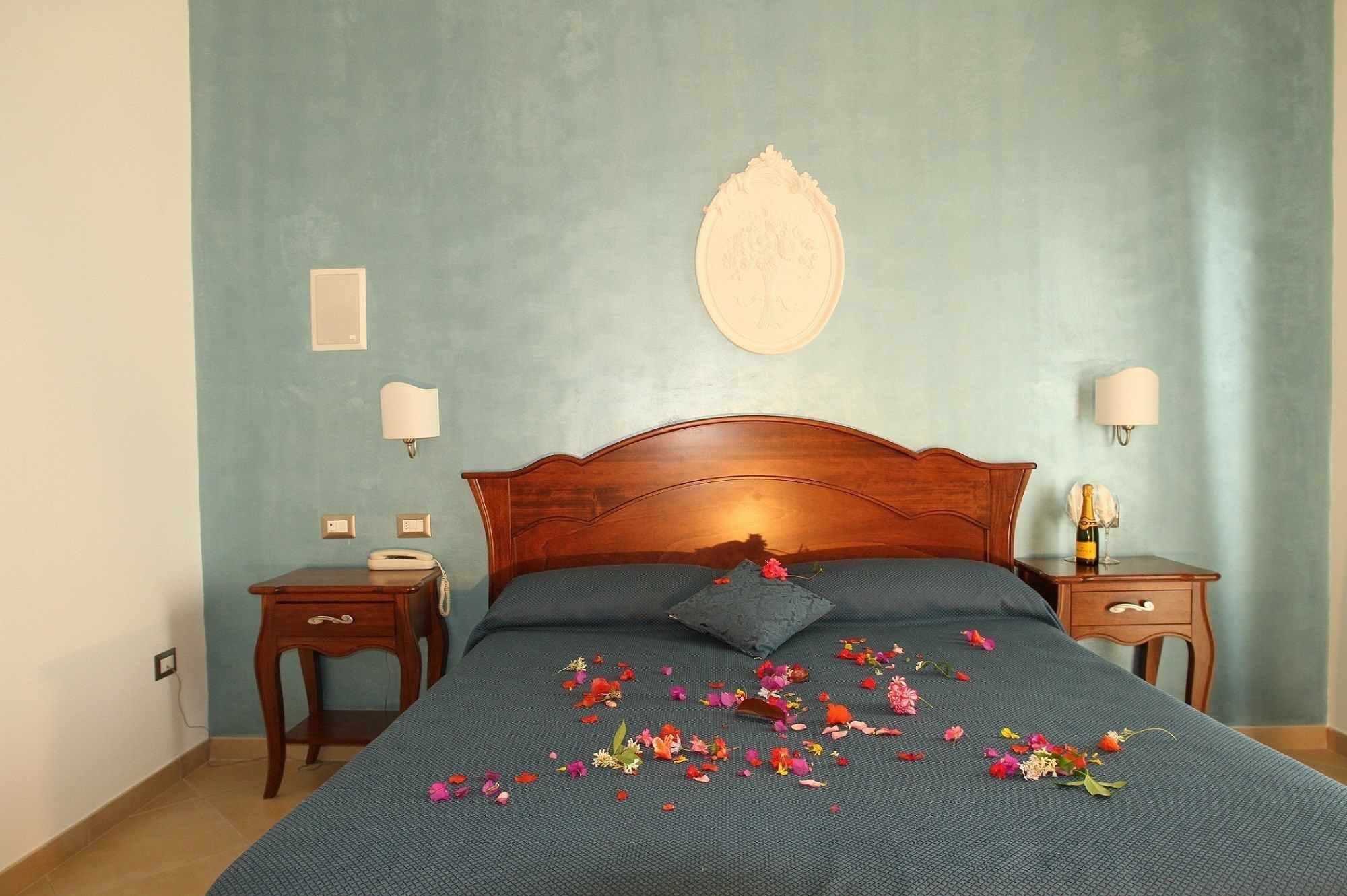Una cama bien hecha con cabecera de madera, dos mesitas de noche con lámparas y un adorno decorativo sobre la cama.