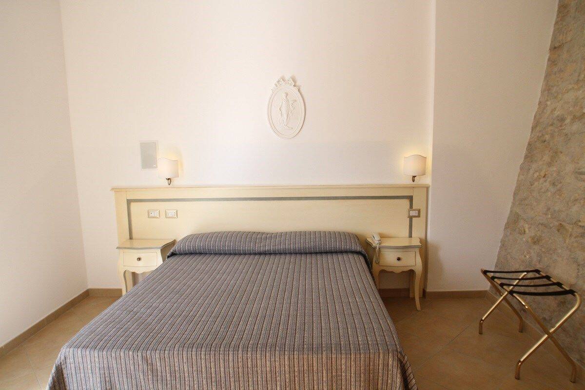 A neatly made bed with a striped bedspread, two bedside lamps, a wall-mounted decorative piece, and a small table with a lamp.