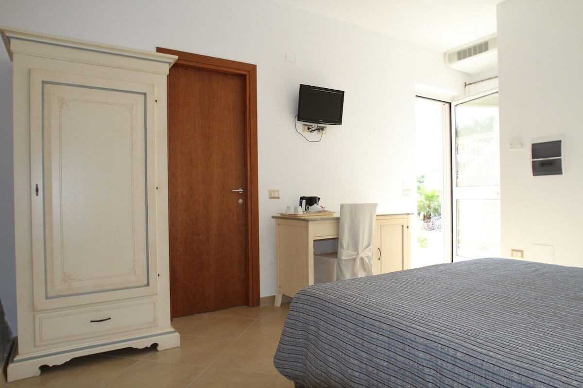 A bedroom with a large wardrobe, a bed, a television mounted on the wall, and a small desk with a chair.