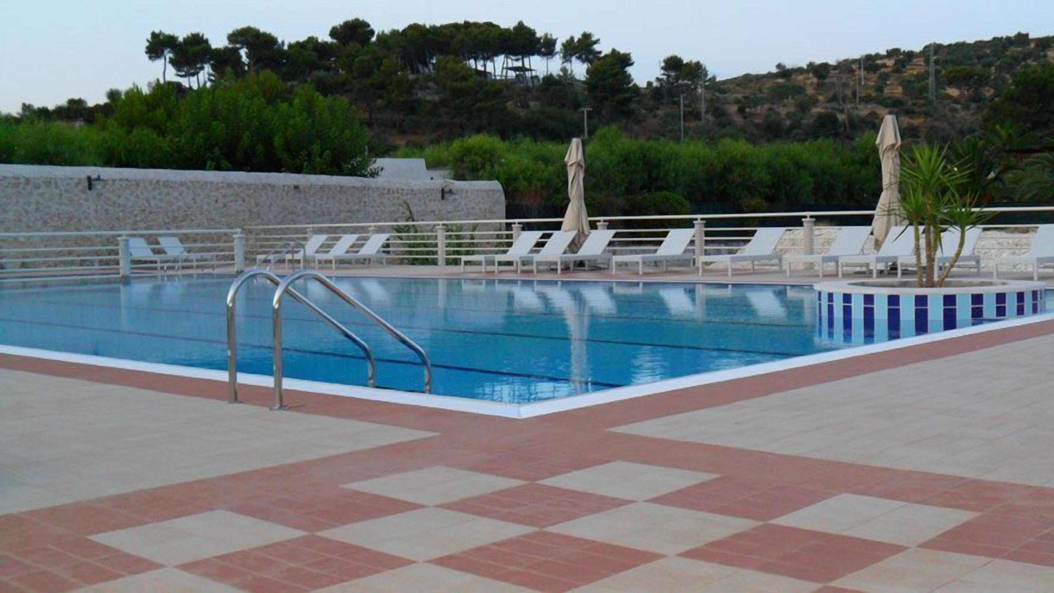 A swimming pool with a tiled deck, lounge chairs, and umbrellas.