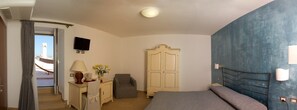 A bedroom with a bed, a desk with a lamp, a chair, a wardrobe, and a TV on the wall. - Hotel Il Castellino Relais (Vieste)
