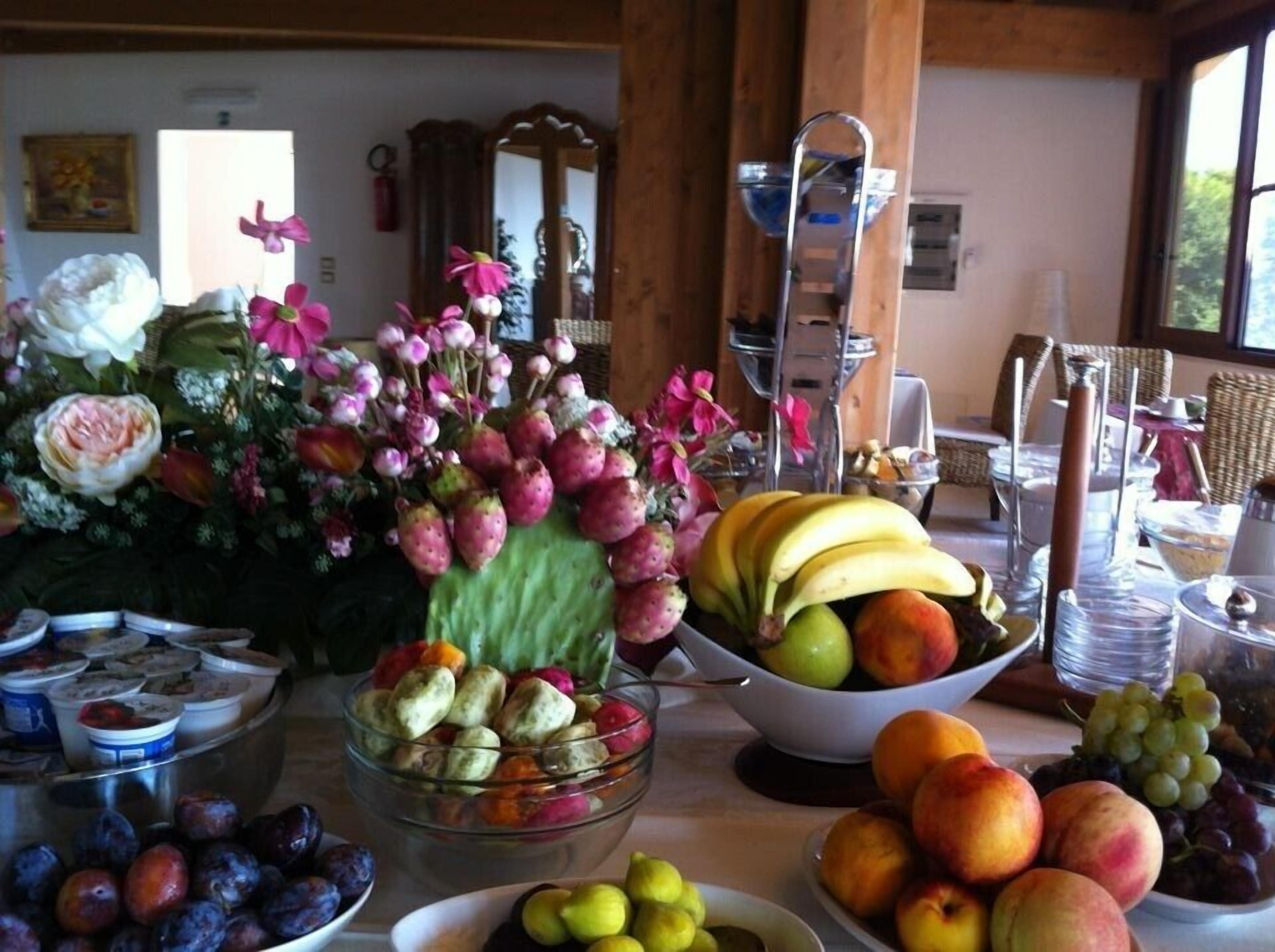 Taula amb diverses fruites, un bol de pastissos i un ram de flors.