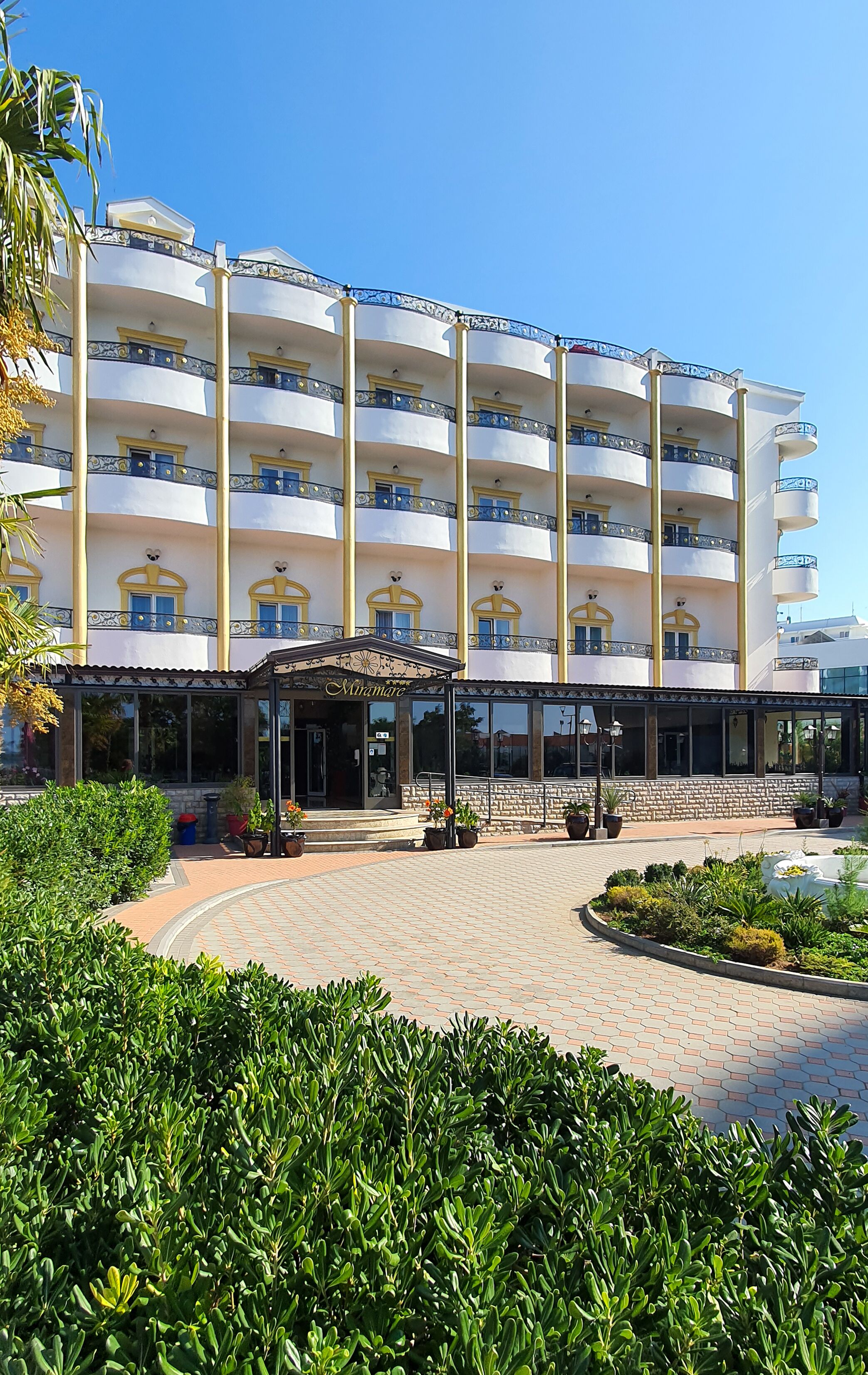 Un hotel de varios pisos con un patio central, plantas en macetas y un acceso cubierto.